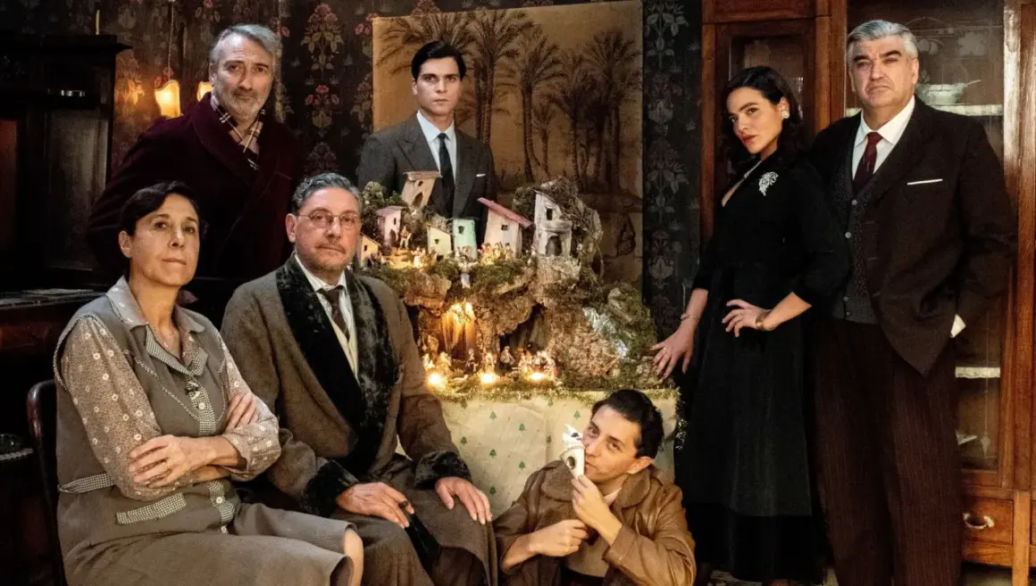 Il cast del film "Natale in casa Cupiello" posa davanti a un presepe illuminato.
