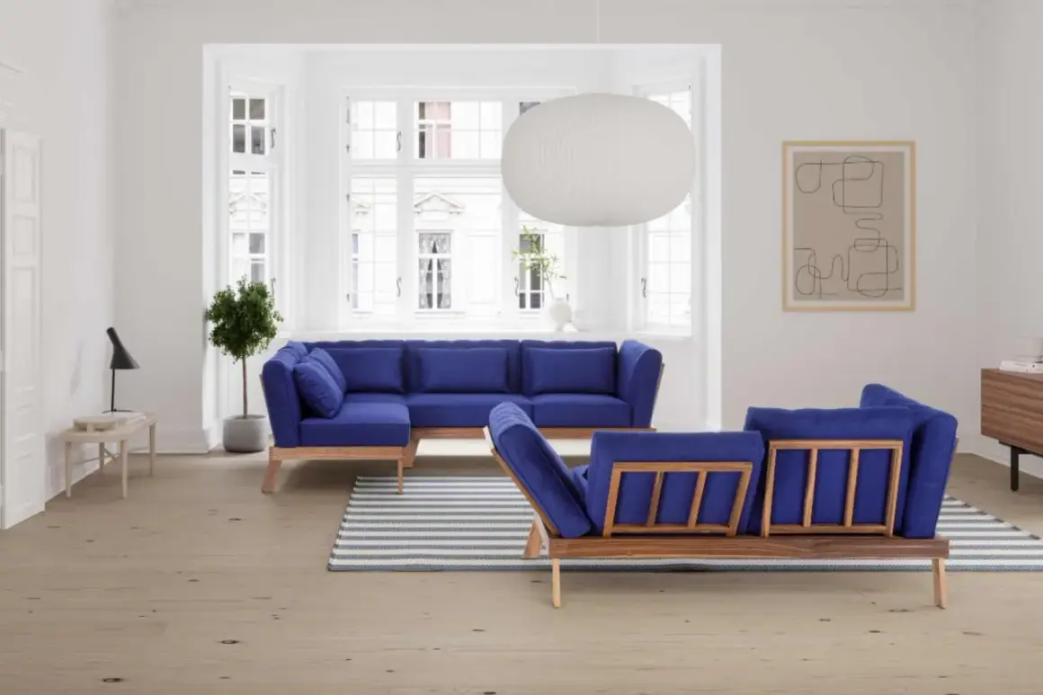 Ein tiefblaues Sofa mitten im Raum, mit Holzrahmen und passenden Kissen. Ein Streifen-Teppich liegt davor.