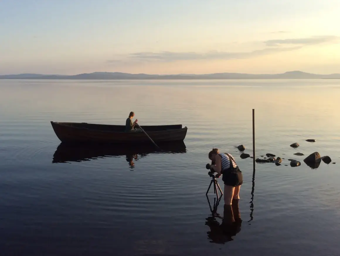 Nygårds Karin Bengtsson filmar en person i en roddbåt vid solnedgången på en lugn sjö.