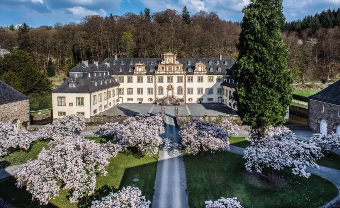 Schloss Ehreshoven erstrahlt im Frühling, umgeben von blühenden Magnolien und einem majestätischen Nadelbaum.