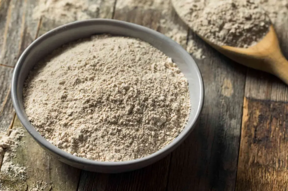 Un bol de farine complète, un équivalent de farine 00 pour des recettes rustiques. Une cuillère en bois en arrière-plan.