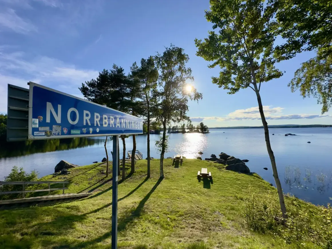 Vacker rastplats vid Norrbränningen, E4 norrut. Solen skiner över sjön, med picknickbord och en brygga.