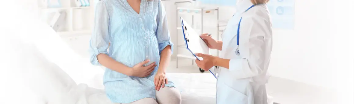 Lekarz spisuje dokumentację medyczną dla ciężarnej kobiety. Dowiedz się, co przysługuje kobiecie w ciąży bez pracy.