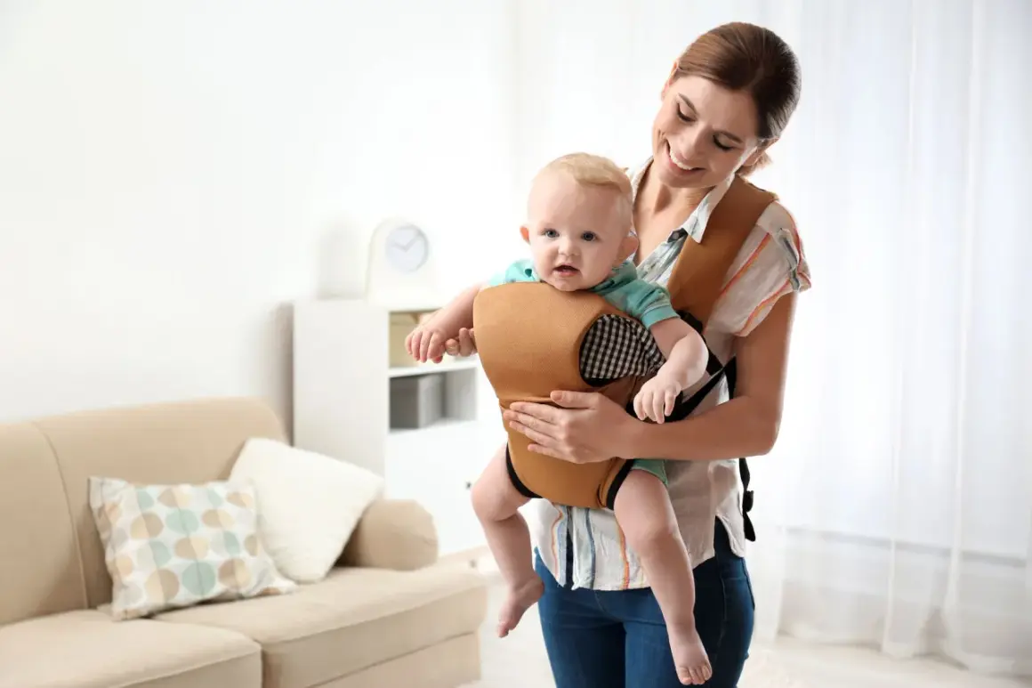 Uśmiechnięta mama trzyma dziecko w wygodnym nosidle. To alternatywa dla chusty, zapewniająca komfort i bezpieczeństwo.