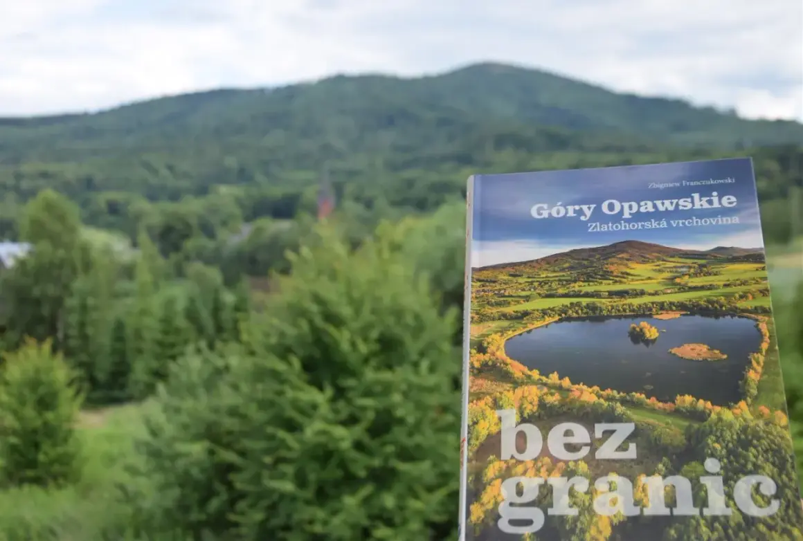 Książka "Góry Opawskie" na tle zielonych wzgórz. Okładka przedstawia malowniczy krajobraz z jeziorem i jesiennymi barwami.