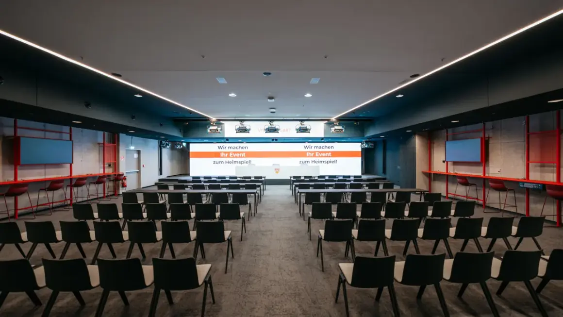 Moderne Konferenzräume im Kulturhaus Arena, bereit für Ihr Event. Reihenweise Stühle und eine große Leinwand mit der Botschaft "Wir machen Ihr Event zum Heimspiel!".