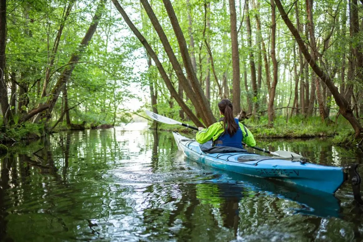 Frau paddelt im Kajak durch einen grünen Wald. Perfekt für Kanutouren NRW.