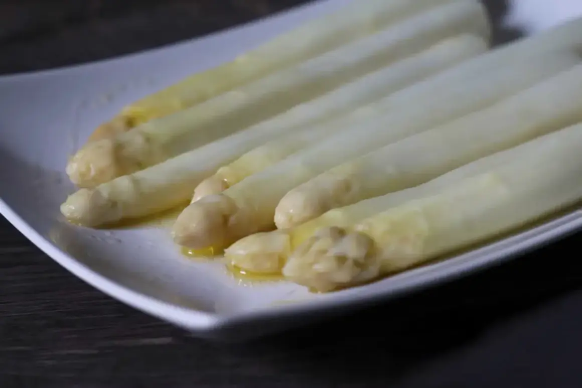 Zarte Spargelspitzen, perfekt gegart im Sous-Vide-Verfahren, liegen auf einer weißen Platte und glänzen in Butter.