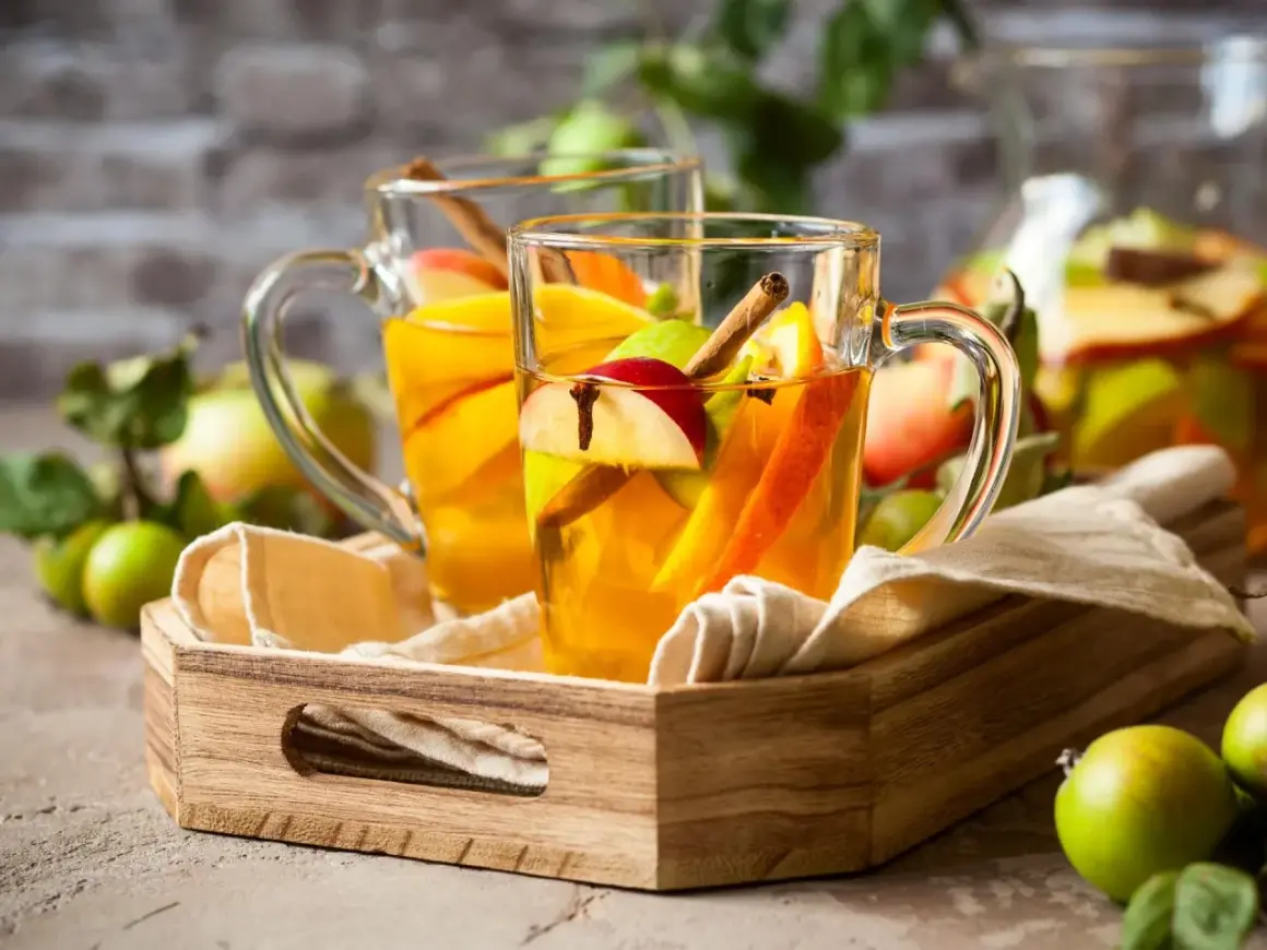 Zwei Gläser mit warmem Apfel-Zimt-Wasser, garniert mit Apfelstücken und Zimtstangen, stehen auf einem Holzteller.