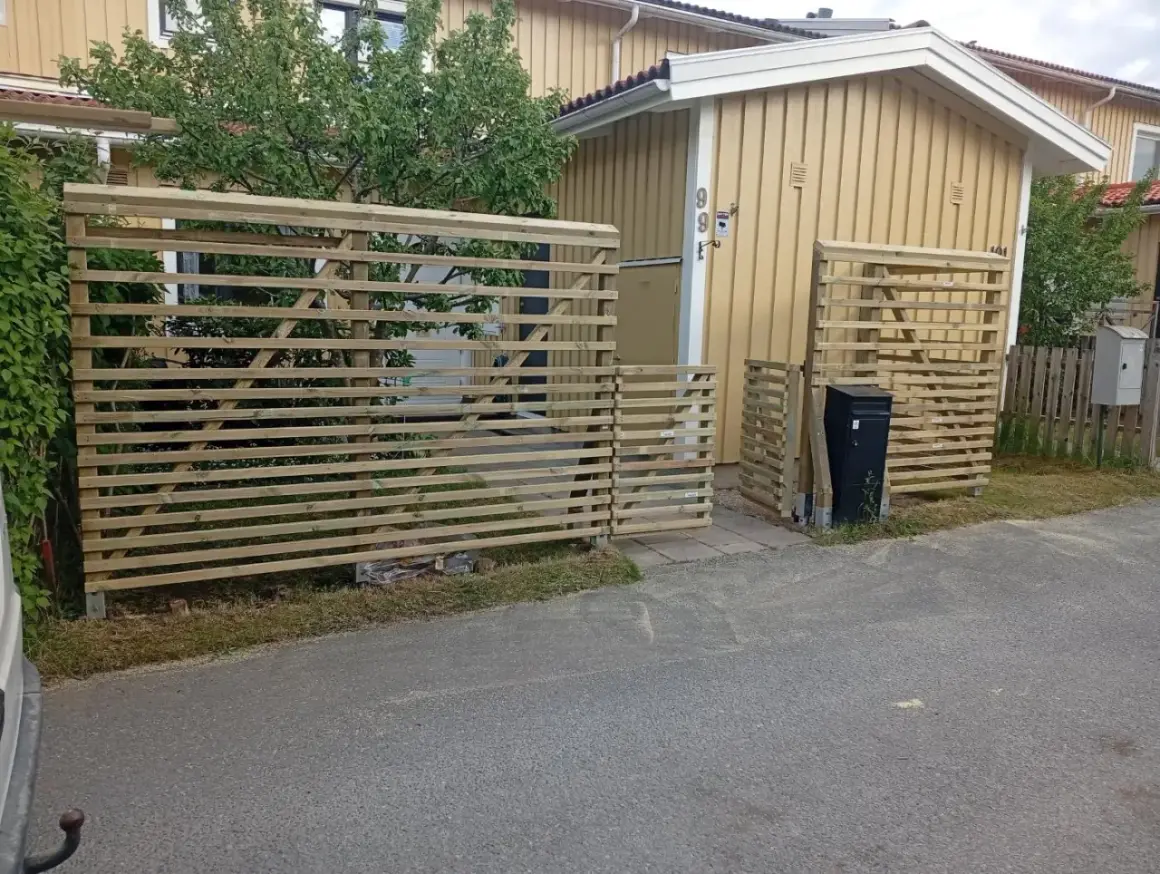Nya trästaket byggs för att bygga insynsskydd vid ett gult hus.