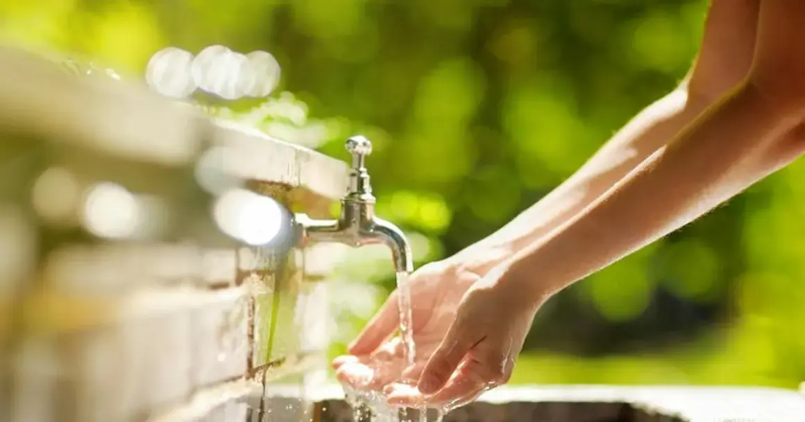 Mains sous un robinet extérieur. La hauteur du robinet extérieur est idéale pour se laver les mains dans ce cadre verdoyant.