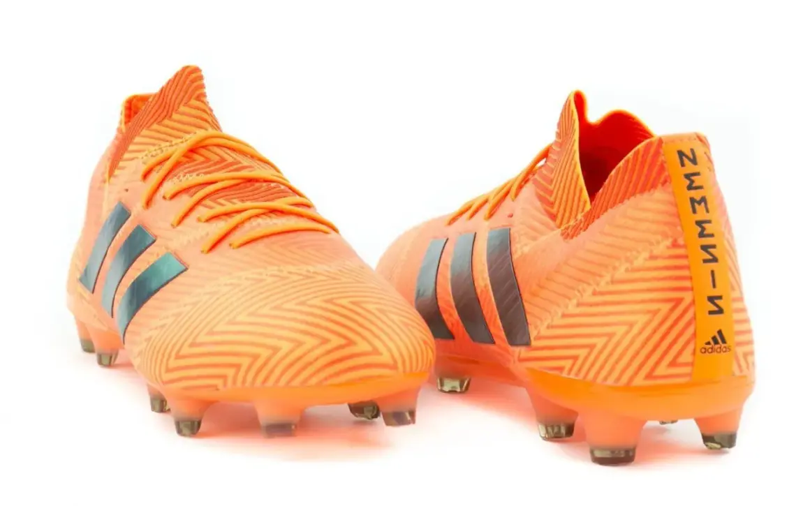Pomarańczowe buty piłkarskie adidas Nemeziz 18.1 z czarnymi paskami i wzorem zygzak.