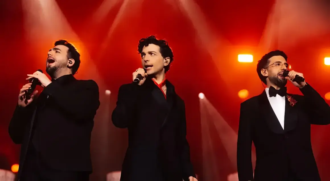 Il trio delle meraviglie, tre cantanti in abiti eleganti, si esibiscono sul palco illuminato da luci rosse.