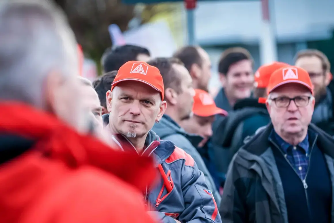 Männer in roten Kappen mit IG Metall Logo, diskutieren über die leistungszulage.