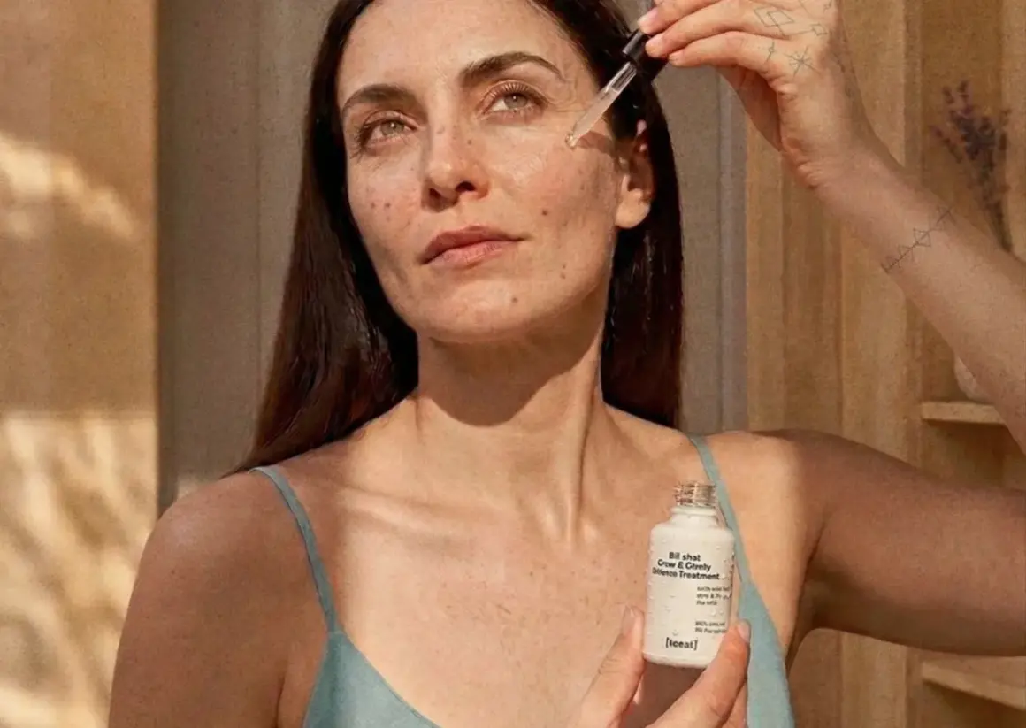 Kobieta aplikuje serum z niacynamidem i witaminą C na skórę. Produkt w białej buteleczce z pipetą.