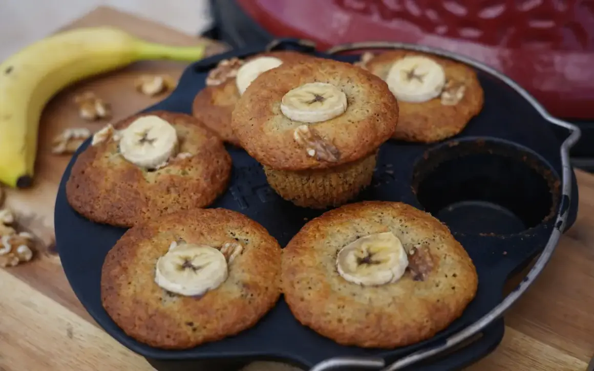 Frisch gebackene Bananen Nuss Muffins, garniert mit Bananenscheiben und Walnüssen, liegen in einer Muffinform.