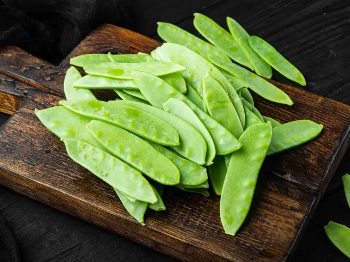 Un mucchio di taccole fresche, verdi e piatte, su un tagliere di legno scuro. Cosa sono? Deliziose!