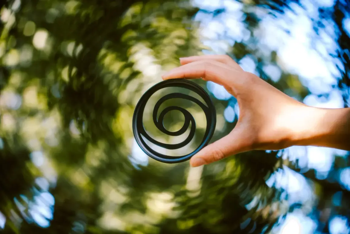 A hand holds a circular filter with a swirly bokeh pattern, creating a vortex of light and color.