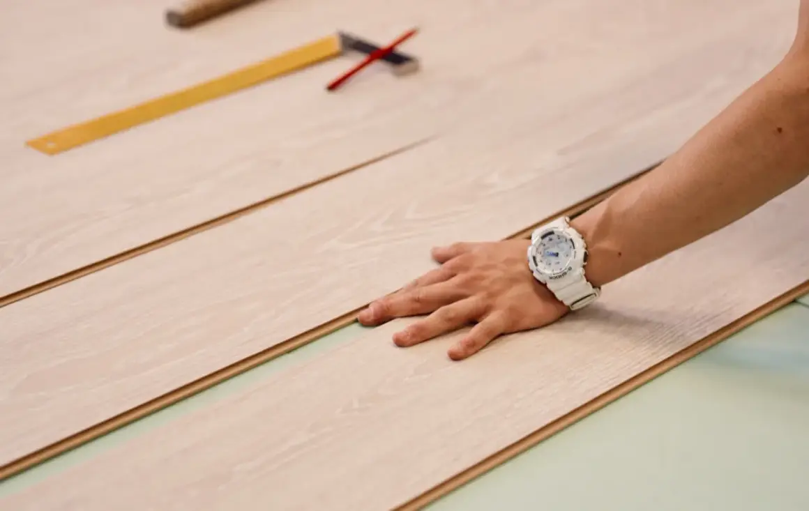 Mano con orologio bianco posata su pannelli di parquet chiaro, pronti per essere tagliati.