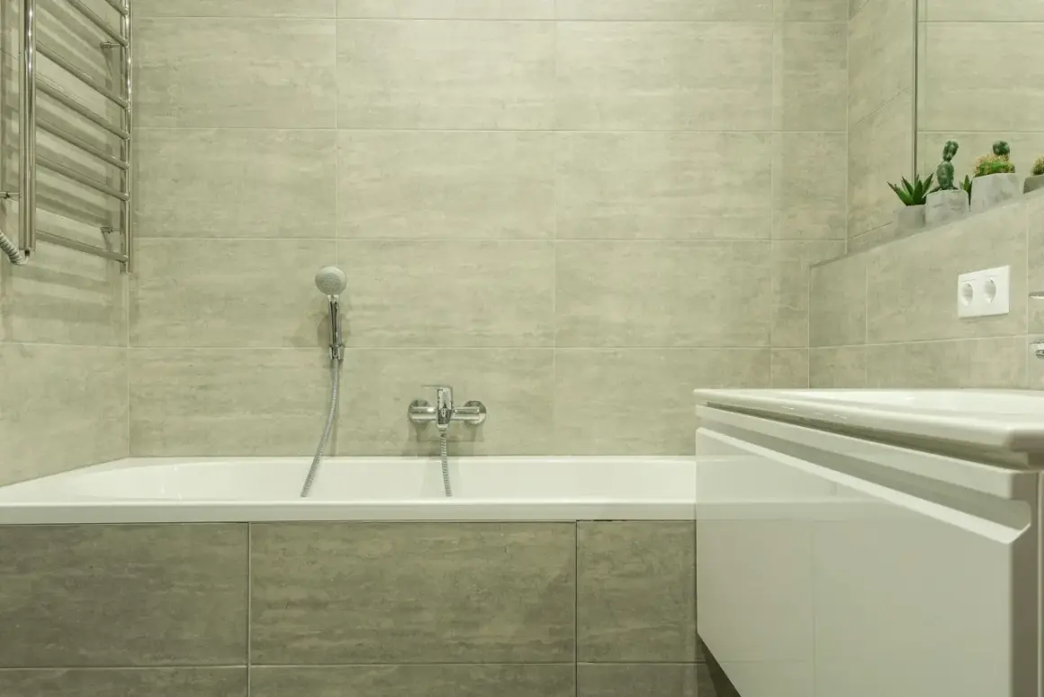 Salle de bain moderne avec baignoire blanche, carrelage gris clair et porte-serviettes chromé. Idéal pour apprendre comment rénover une baignoire.
