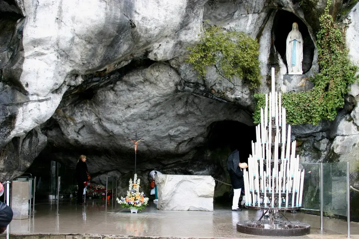 Pilger beten in der Lourdes Grotte Bernadette. Eine Marienstatue und Kerzen stehen in der Höhle.