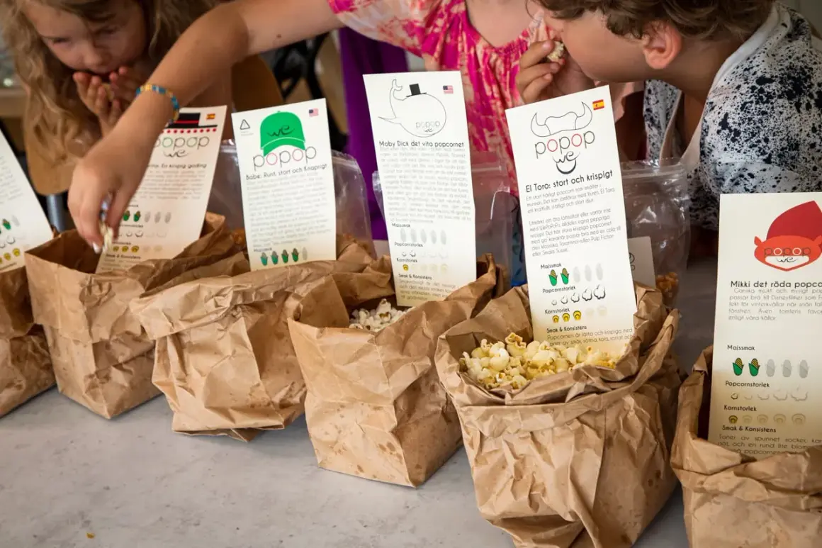 Barn plockar popcorn ur papperspåsar. En påse med popcorn med kolasås syns tydligt.