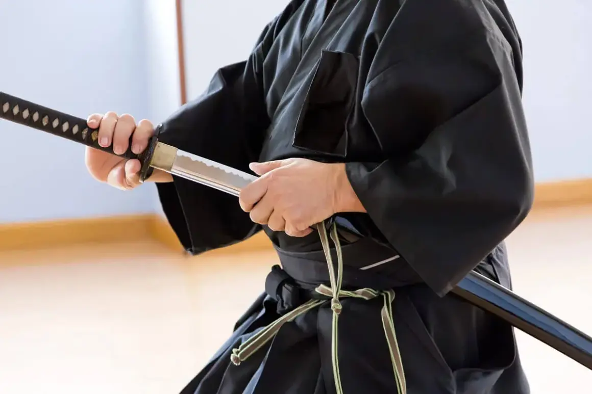 En person i svart dräkt håller ett samurajsvärd, en symbol för japanska krigare.