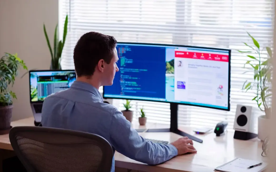 Uomo al lavoro, con la sua postazione schermo PC ottimale per la produttività.