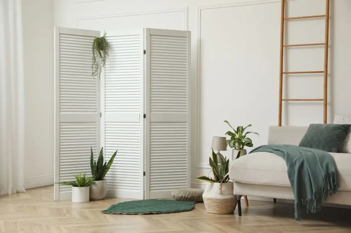 Weißer Klapp-Raumteiler mit Pflanzen und Sofa in hellem Wohnbereich.