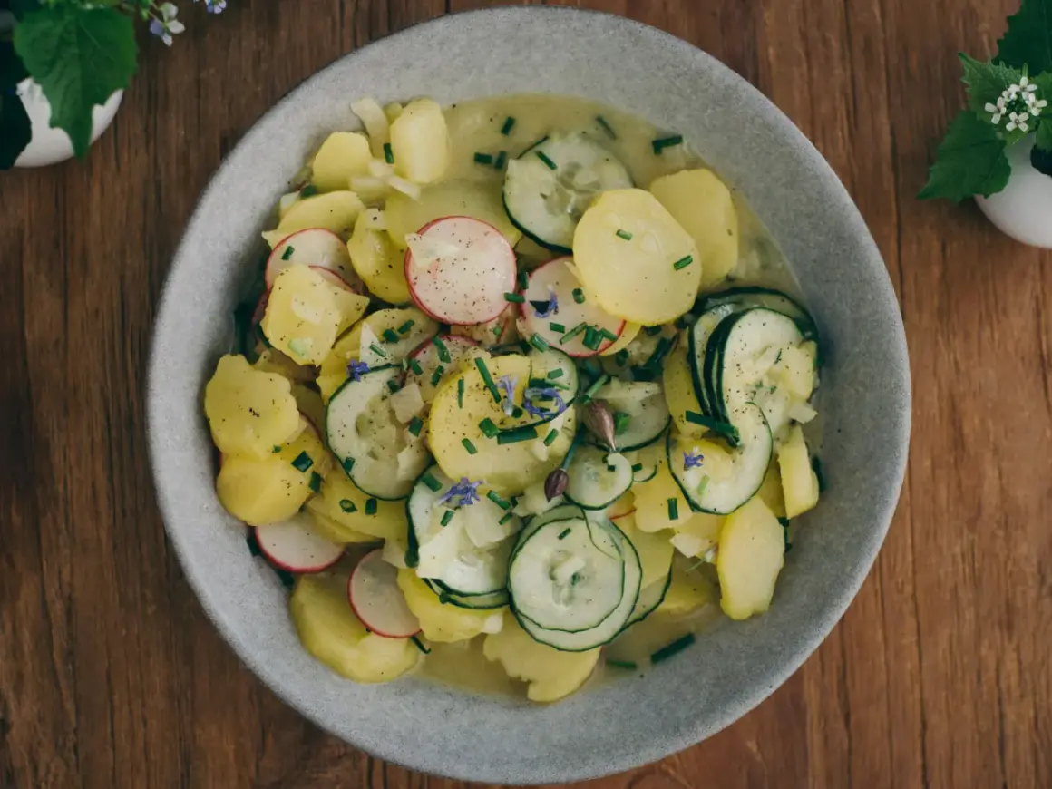 Ein Teller mit traditionellem bayrischem Kartoffelsalat, garniert mit Radieschen, Gurken und Schnittlauch.