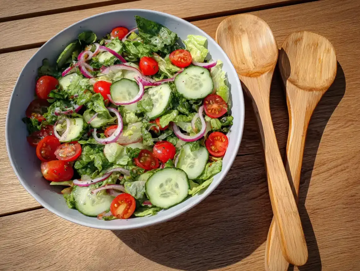 En fräsch sallad med tomater, gurka och rödlök, perfekt som sallad till grillat. Två träskedar ligger bredvid.