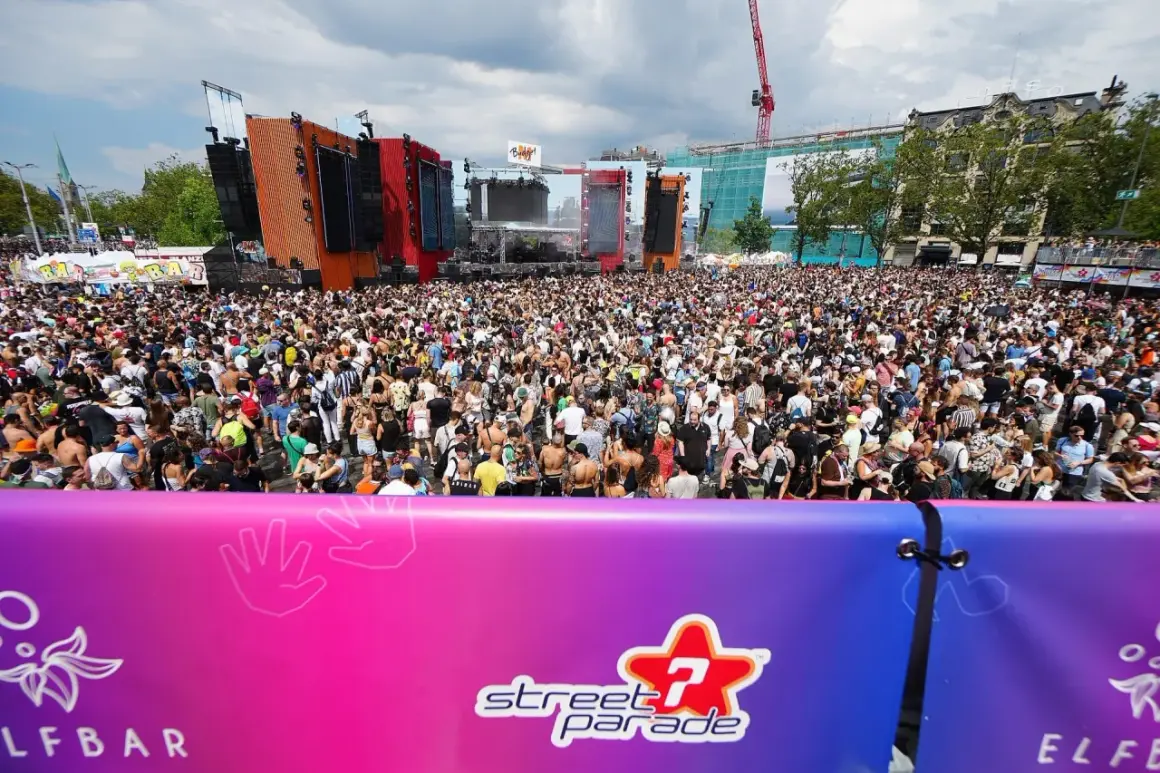 Folla immensa al festival techno di Zurigo, Street Parade, con DJ set e musica elettronica sotto un cielo nuvoloso.