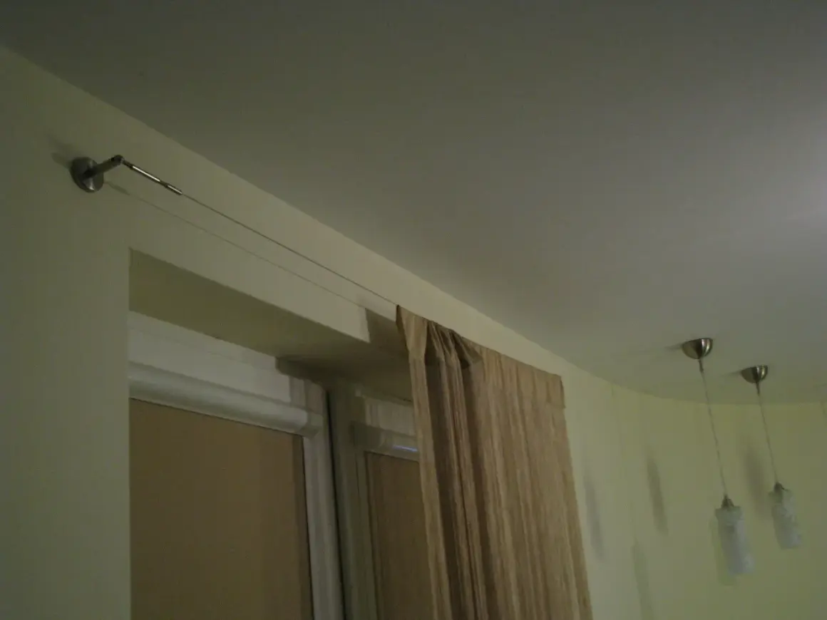 Elegancka zasłona w beżowym kolorze wisi na cienkiej lince zamiast karnisza, tworząc minimalistyczny wygląd.