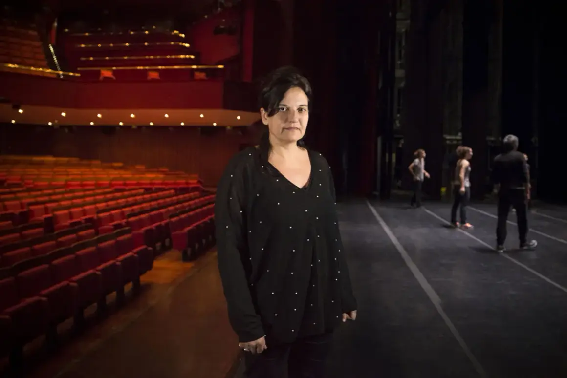 Emma Dante in un teatro, con le poltrone rosse vuote e il palco illuminato.