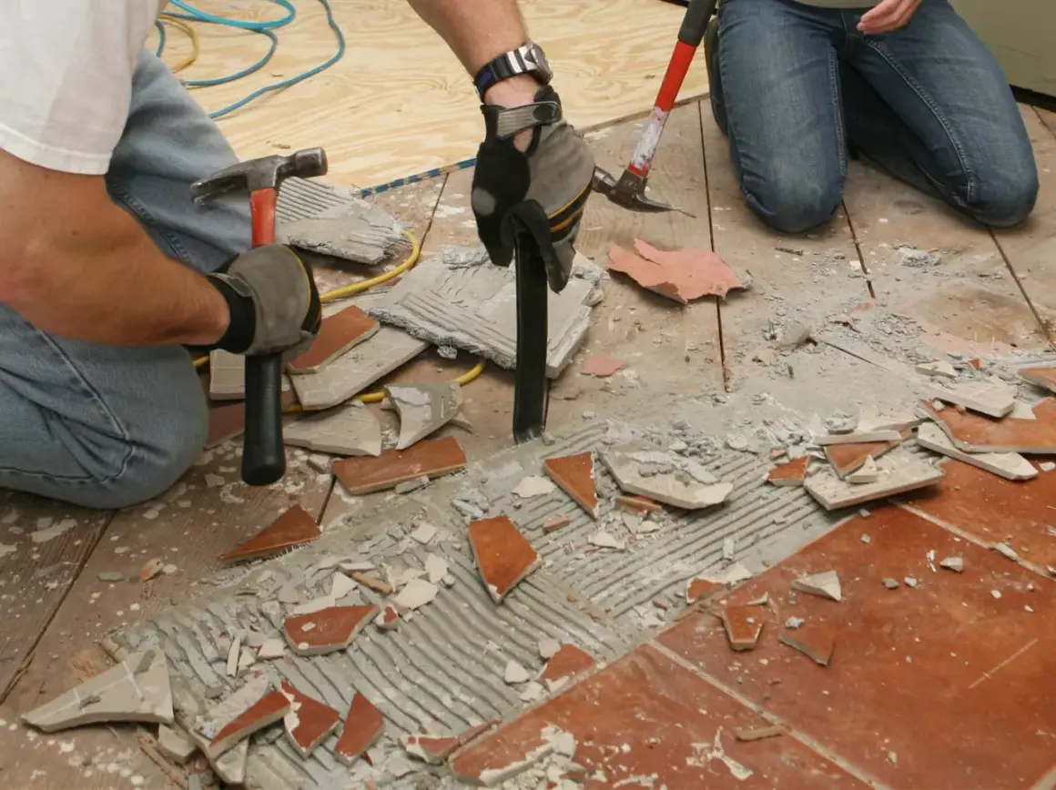Deux personnes s'y prennent pour comment décoller du carrelage au sol, utilisant marteaux et burins pour briser les carreaux et le ciment.