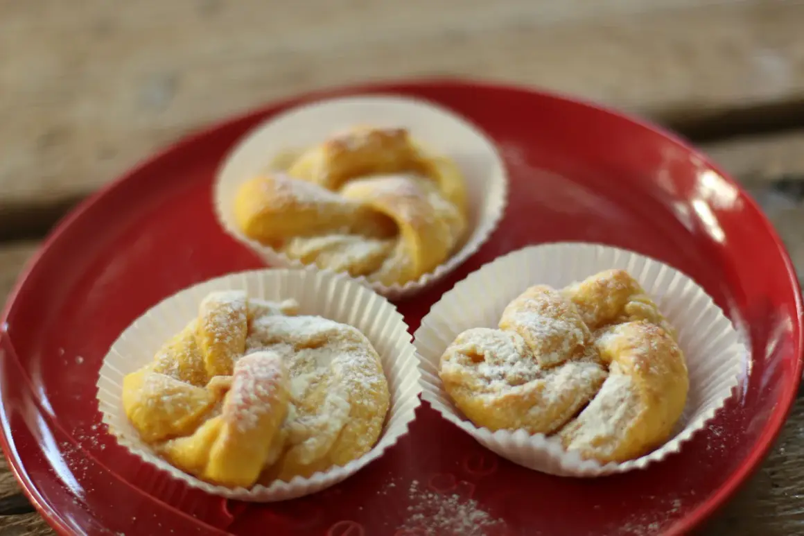 Tre saffransbullar med vit choklad, pudrade med florsocker, ligger på en röd tallrik.