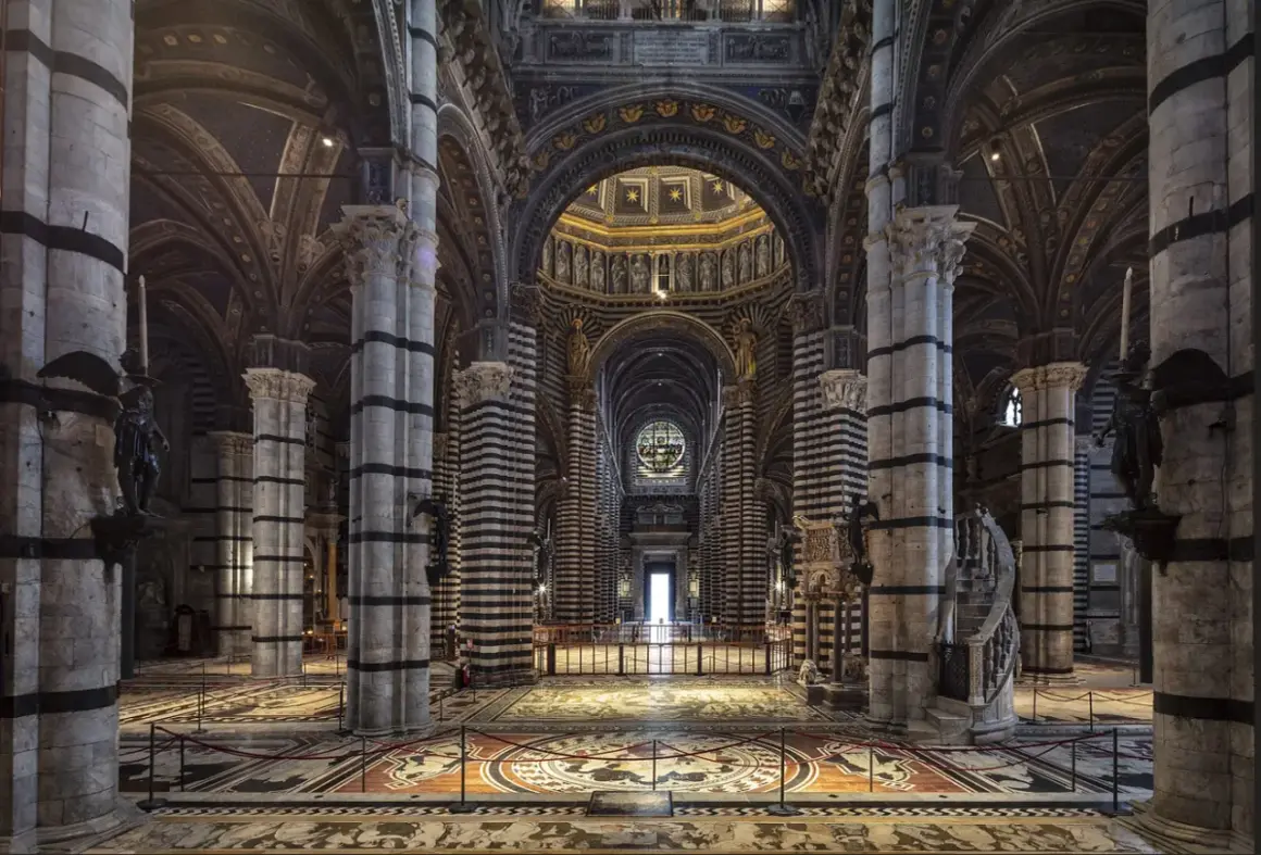 Interno del Duomo di Siena, con il suo magnifico pavimento intarsiato e le colonne a strisce bianche e nere che conducono verso l'altare.