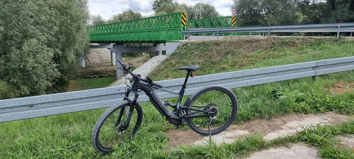Rower elektryczny czeka na przygodę na trasie w Kazimierzu Dolnym. Zielony most w tle zaprasza do odkrywania malowniczych zakątków.