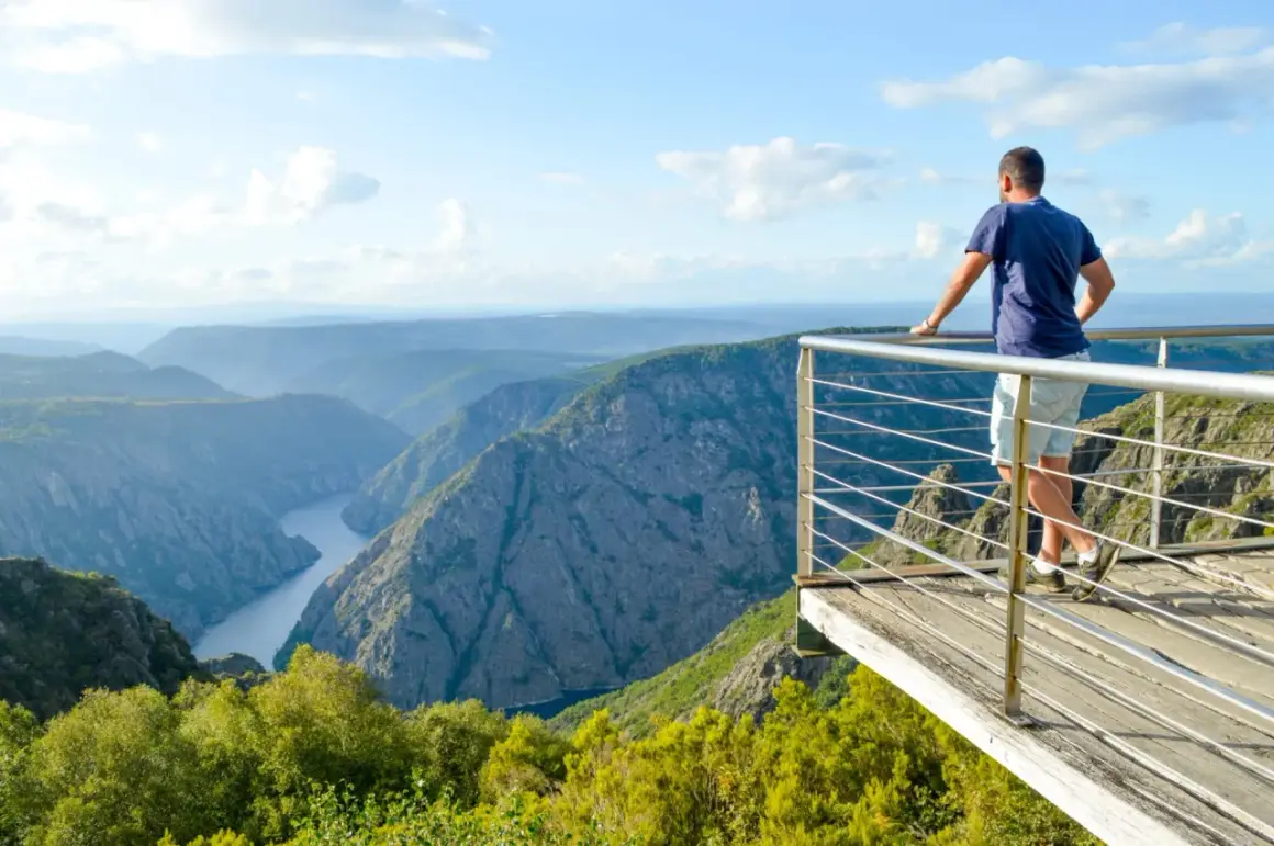 Hombre en el mirador de Cabezoas, contemplando un cañón con un río serpenteante y montañas cubiertas de vegetación.
