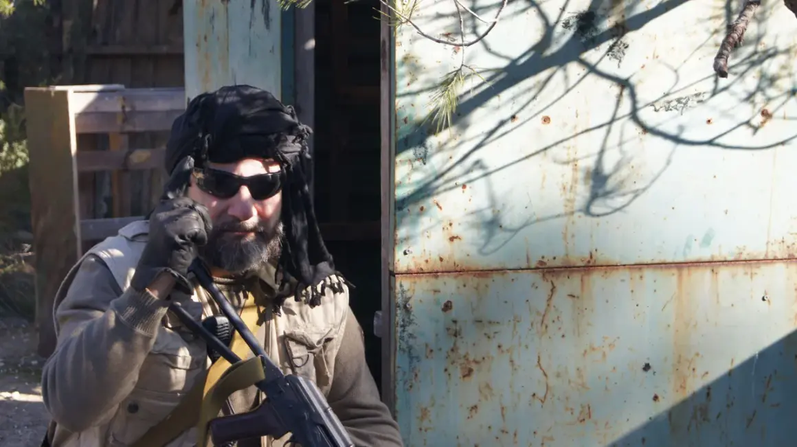 Hombre con turbante negro, gafas de sol y chaleco táctico, listo para una partida de milsim airsoft.
