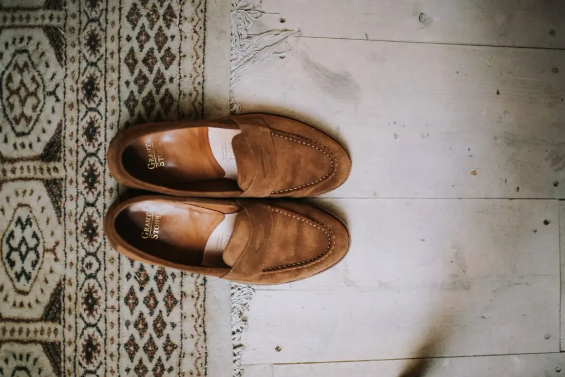 Une paire de mocassins en daim marron, posée sur un tapis à motifs et un parquet. Idéal pour raviver la couleur du daim naturellement.