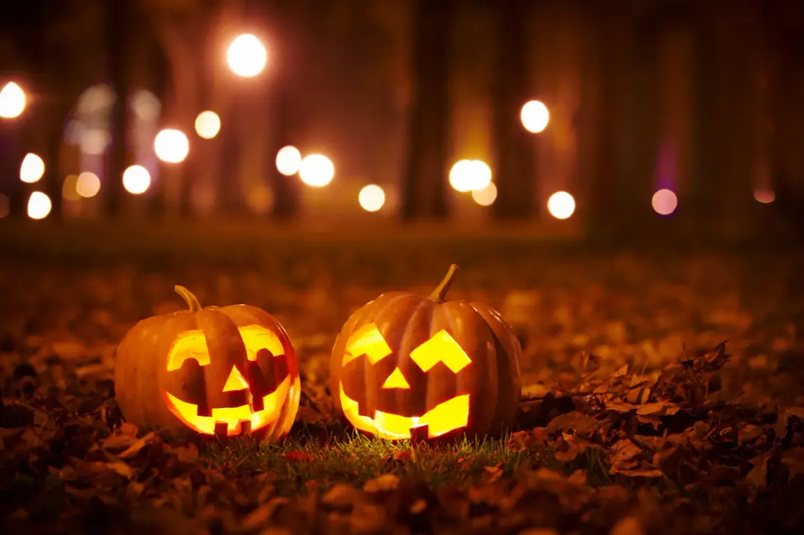 Two carved pumpkins glow with warm light on a bed of fallen leaves, perfect for halloween decorations on the cheap.