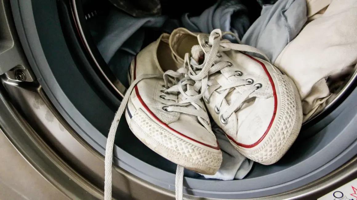 Weiße Turnschuhe mit roten Streifen liegen in der Waschmaschine, bereit zum Laufschuhe waschen.