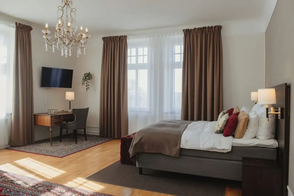 Ett elegant hotellrum på hotel Drott Karlstad med en stor säng, skrivbord och kristallkrona.