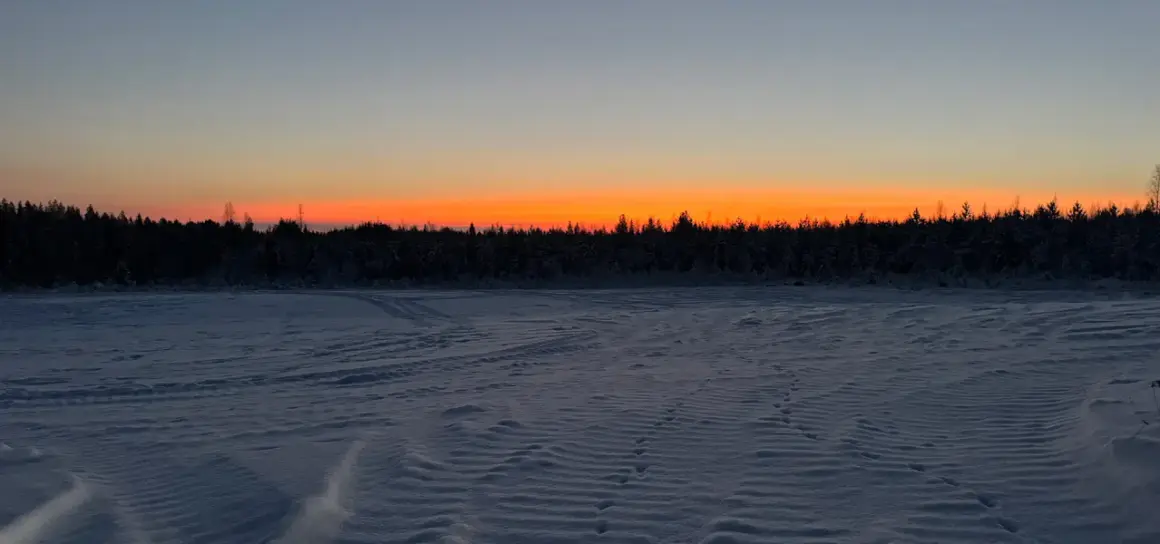 Paisaje invernal con cielo anaranjado al atardecer. Huellas en la nieve sugieren el camino para saber como ir a Laponia.