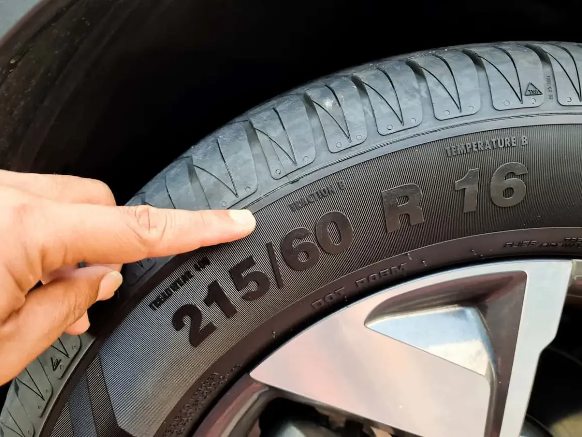Palec wskazuje na oznaczenia opon: 215/60 R16. Informacje te pomagają dobrać odpowiednie ogumienie.