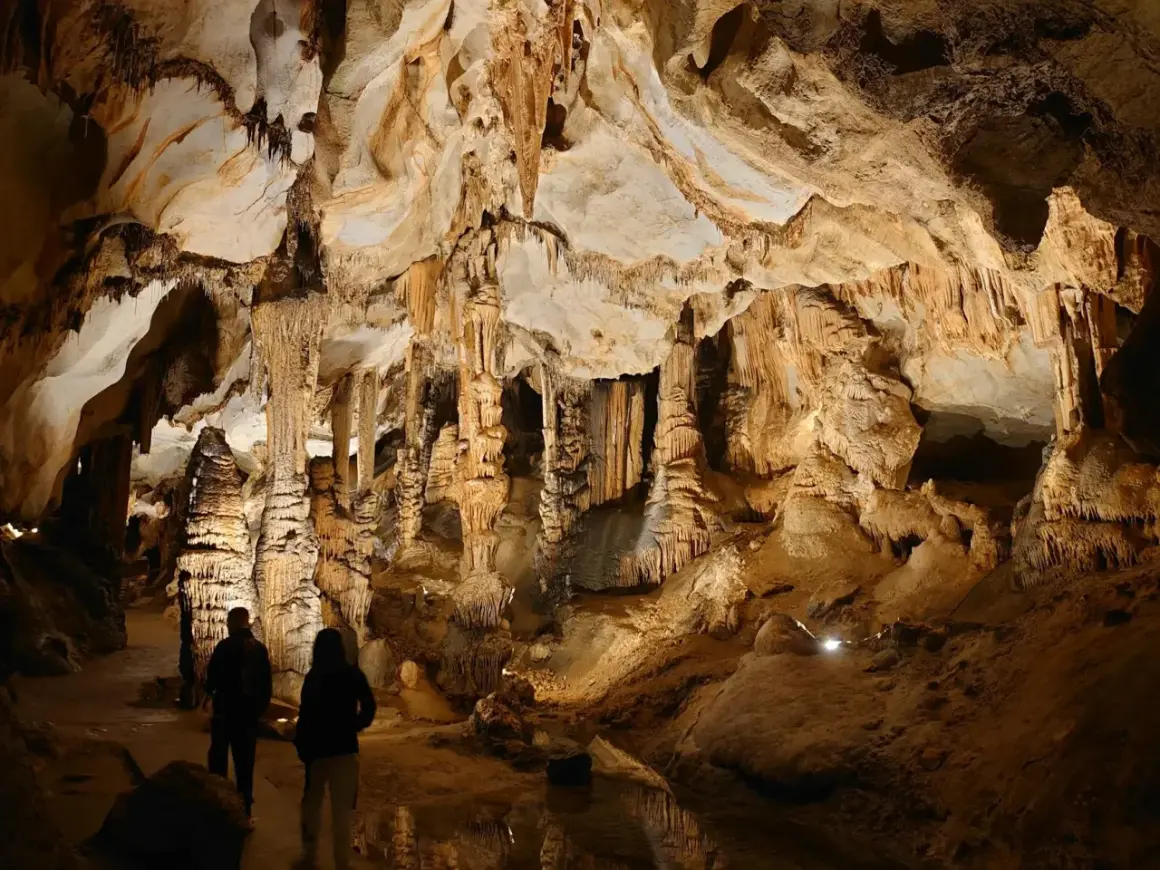 Odkrywanie najpiękniejszych jaskiń w Polsce. Dwie osoby podziwiają imponujące stalaktyty i stalagmity w oświetlonej grocie.