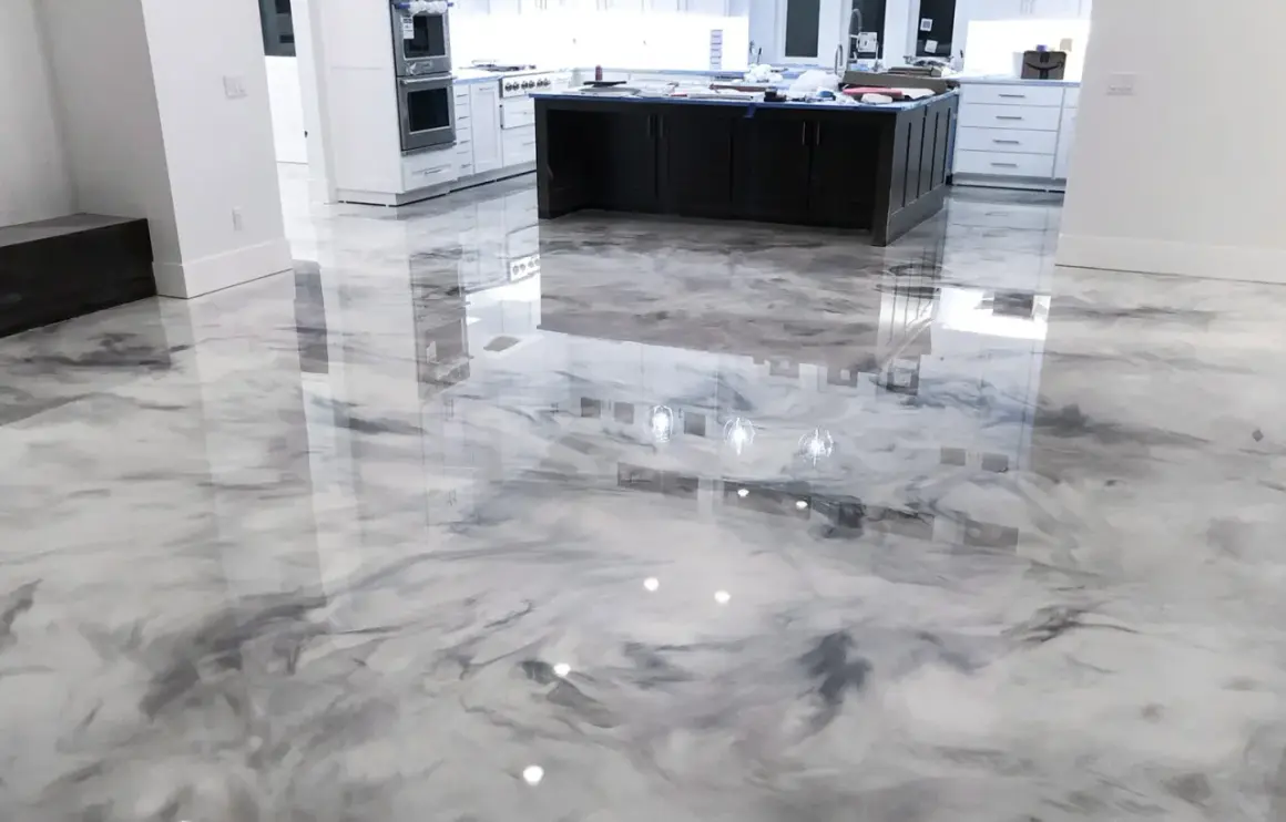 Un moderno pavimento epossidico con un effetto marmorizzato bianco e grigio riflette le luci e l'arredamento della cucina.