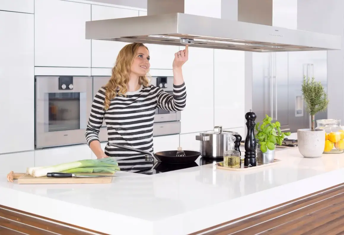 Junge Frau bedient Dunstabzugshaube mit Herd-Abschaltautomatik. Sicheres Kochen für Senioren.