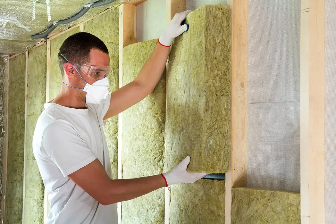 Un ouvrier installe un panneau d'isolation minérale dans une structure murale en bois, respectant les normes d'isolation des murs RT 2020.